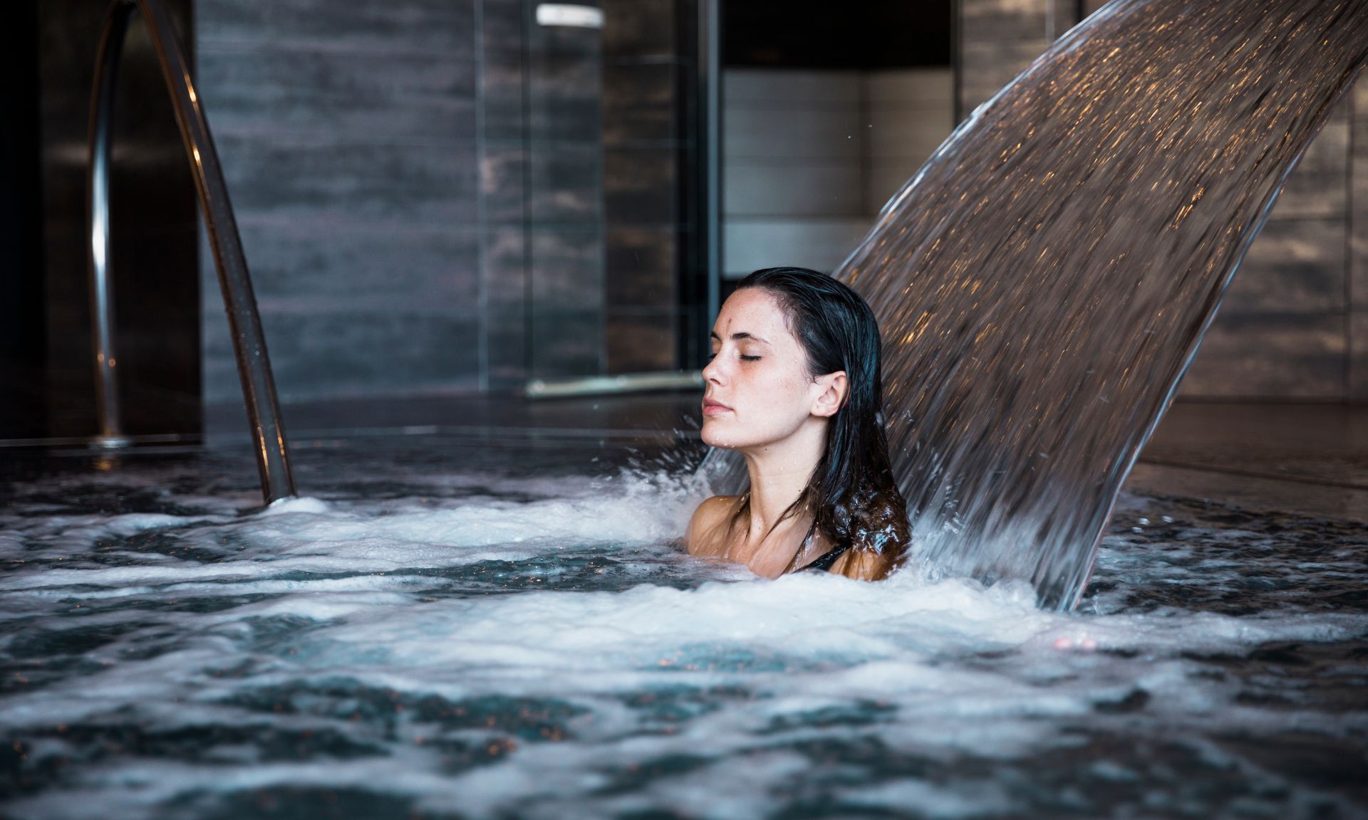 Chica en un spa debajo de una cascada de un spa